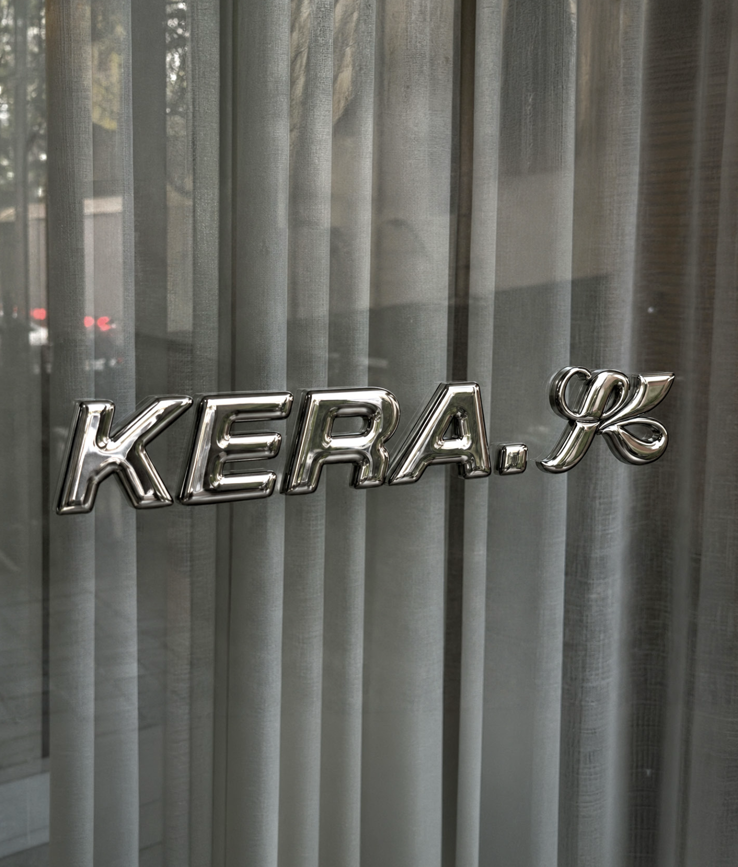 Logo KERA chromé devant des rideaux translucides dans la lumière du studio
